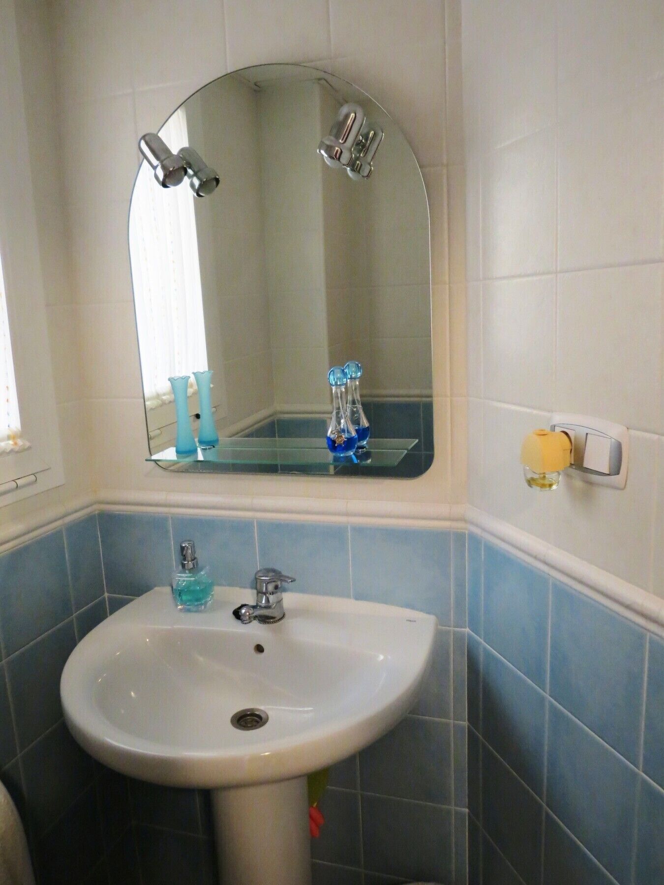 Une salle de bain avec un miroir rond, un lavabo avec un robinet et un distributeur de savon fixé au mur.