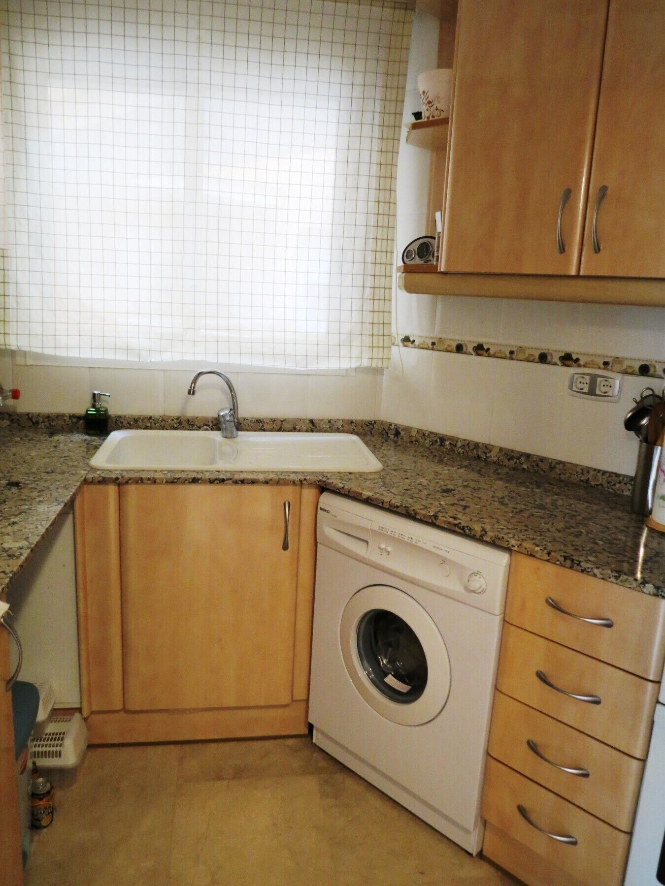 Cocina compacta con lavadora integrada, un lavamanos y armarios de madera.