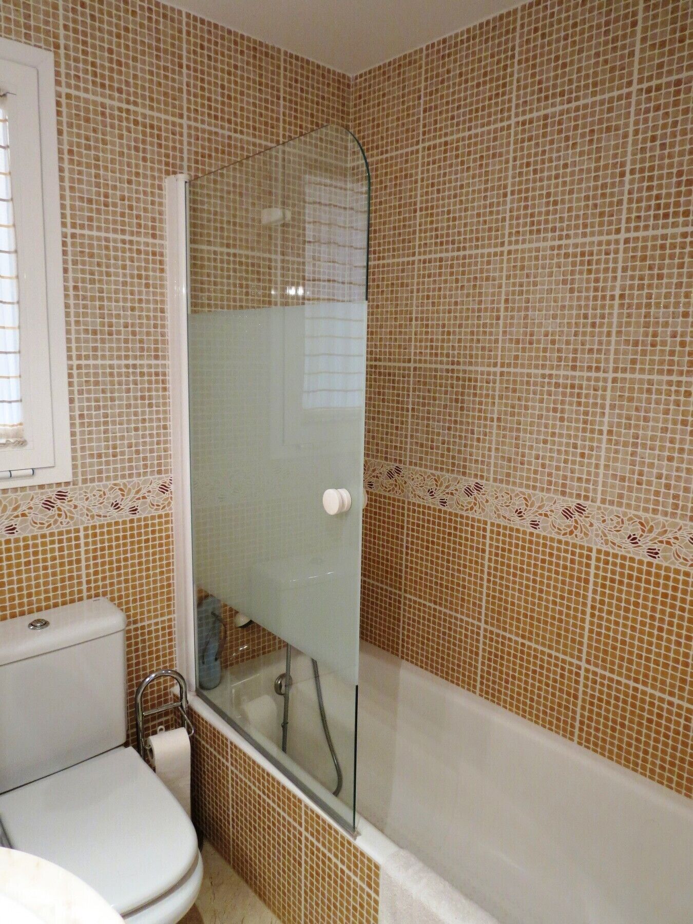 Une salle de bain avec une douche à parois de verre, des toilettes et des murs carrelés.