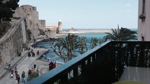 Vista costera con una fortificación de piedra, un paseo marítimo y un cielo azul despejado.