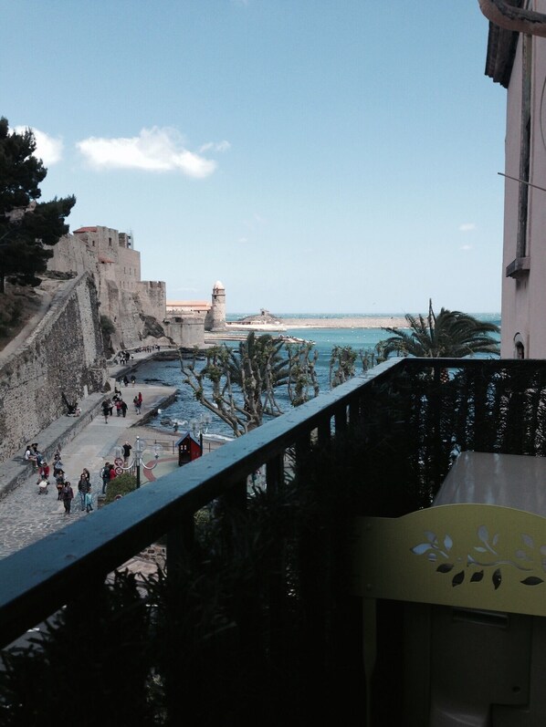 Vista costera con una fortificación de piedra, un paseo marítimo y un cielo azul despejado.