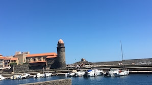 Un pueblo costero con una torre destacada, un puerto con barcos y edificios con tejados rojos.