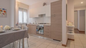 A modern kitchen with white cabinets, a built-in oven, and a dining area with a table set for two. - Alexis House Varenna (Varenna)