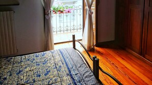 Een slaapkamer met een bed, een houten vloer en uitzicht op een balkon met planten.