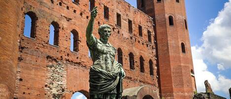 A statue in front of a historic brick building with arched windows and a tower.