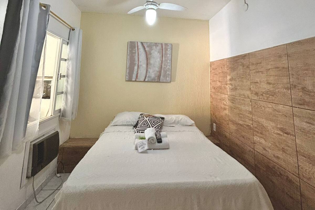 Une chambre d’hôtel avec un lit, un ventilateur de plafond, une fenêtre avec des rideaux et une œuvre d’art accrochée au mur.