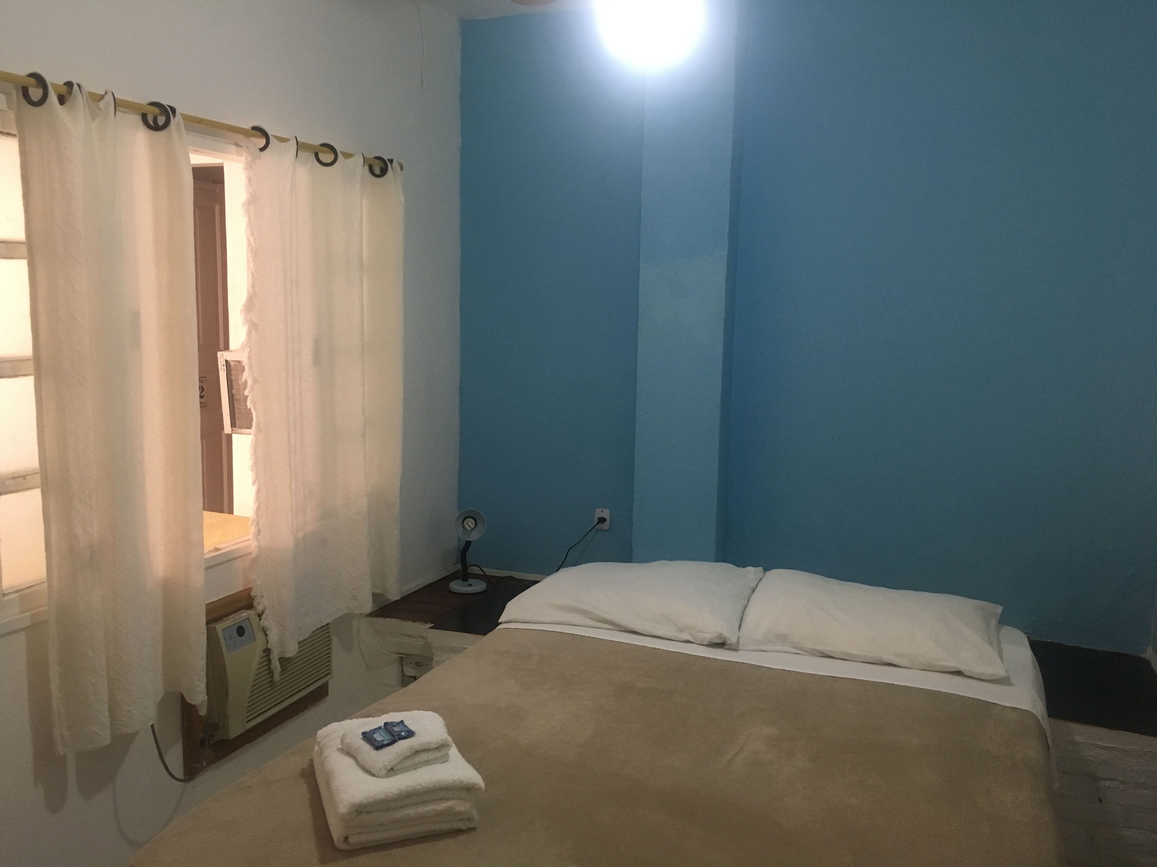 A bedroom with a bed, a bedside table, a heater, and a window with curtains.
