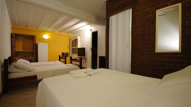A hotel room with two beds, a brick wall, a white door, and a mirror. - Pousada Aldeia Buzios (Búzios)