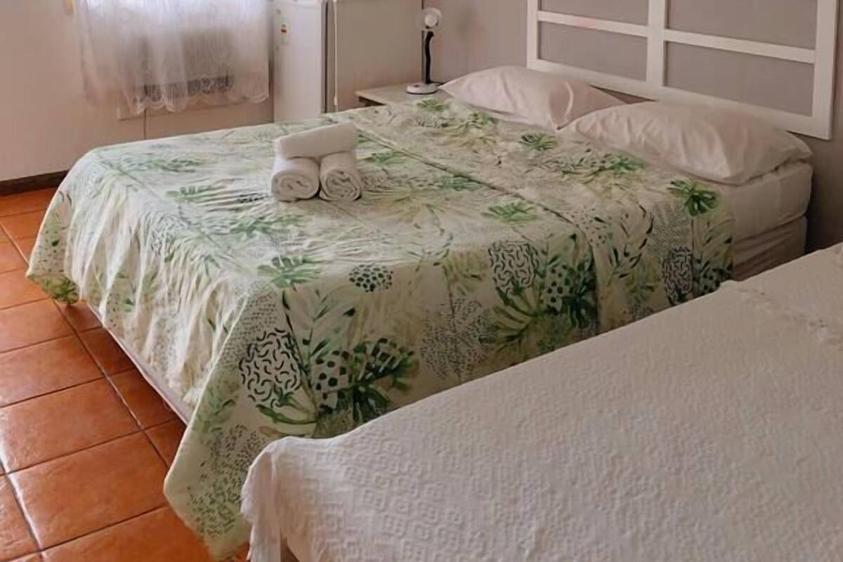 Une chambre avec deux lits, un ventilateur de plafond, une télévision et une fenêtre avec des rideaux légers.