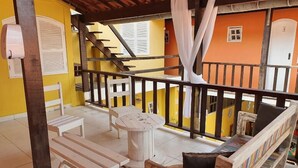 A covered outdoor seating area with wooden benches and tables, a staircase, and a yellow and orange building in the background. - Pousada Aldeia Buzios (Búzios)