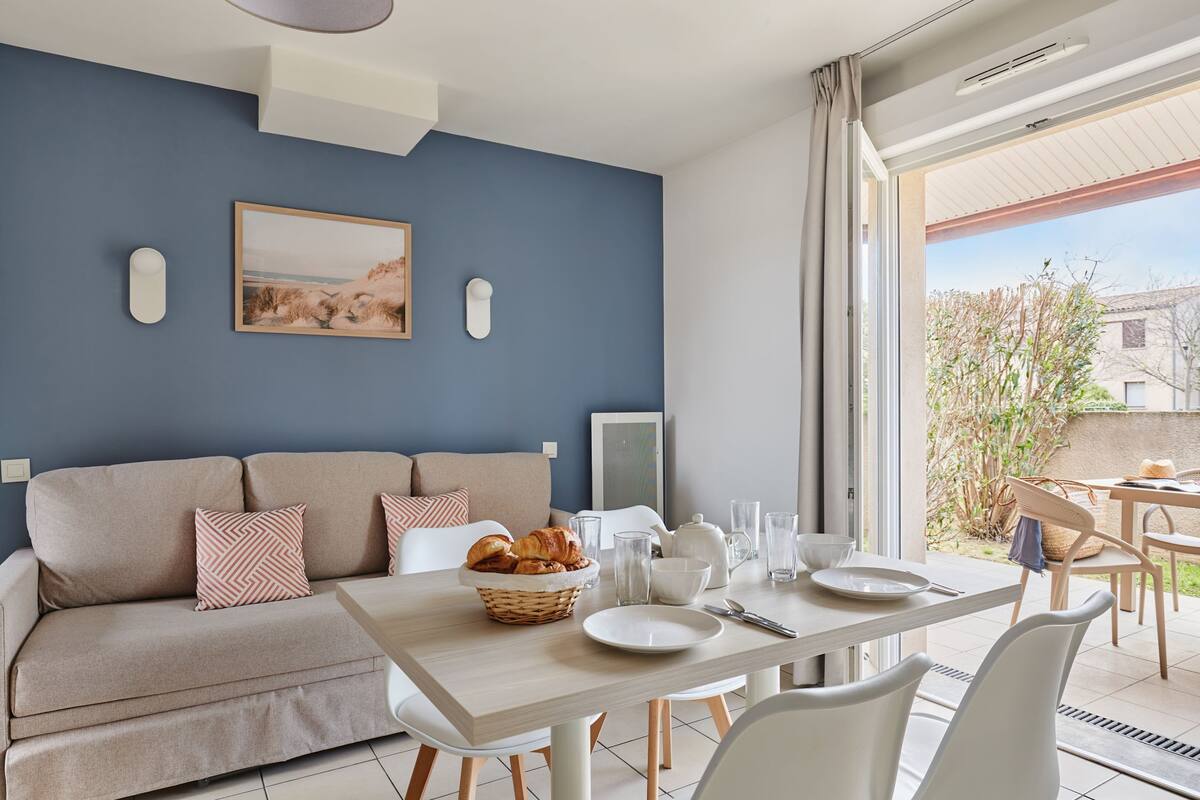 Una sala de estar moderna con un sofá, una mesa de comedor con alimentos para el desayuno y un ventanal con vistas al exterior.
