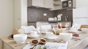 Una cocina moderna con electrodomésticos blancos, una mesa de comedor con vajilla blanca, vasos y una revista.