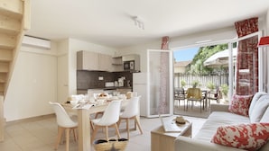 Una cocina moderna con armarios blancos, un comedor con mesa y sillas, y una sala de estar acogedora con un sofá y una computadora portátil.