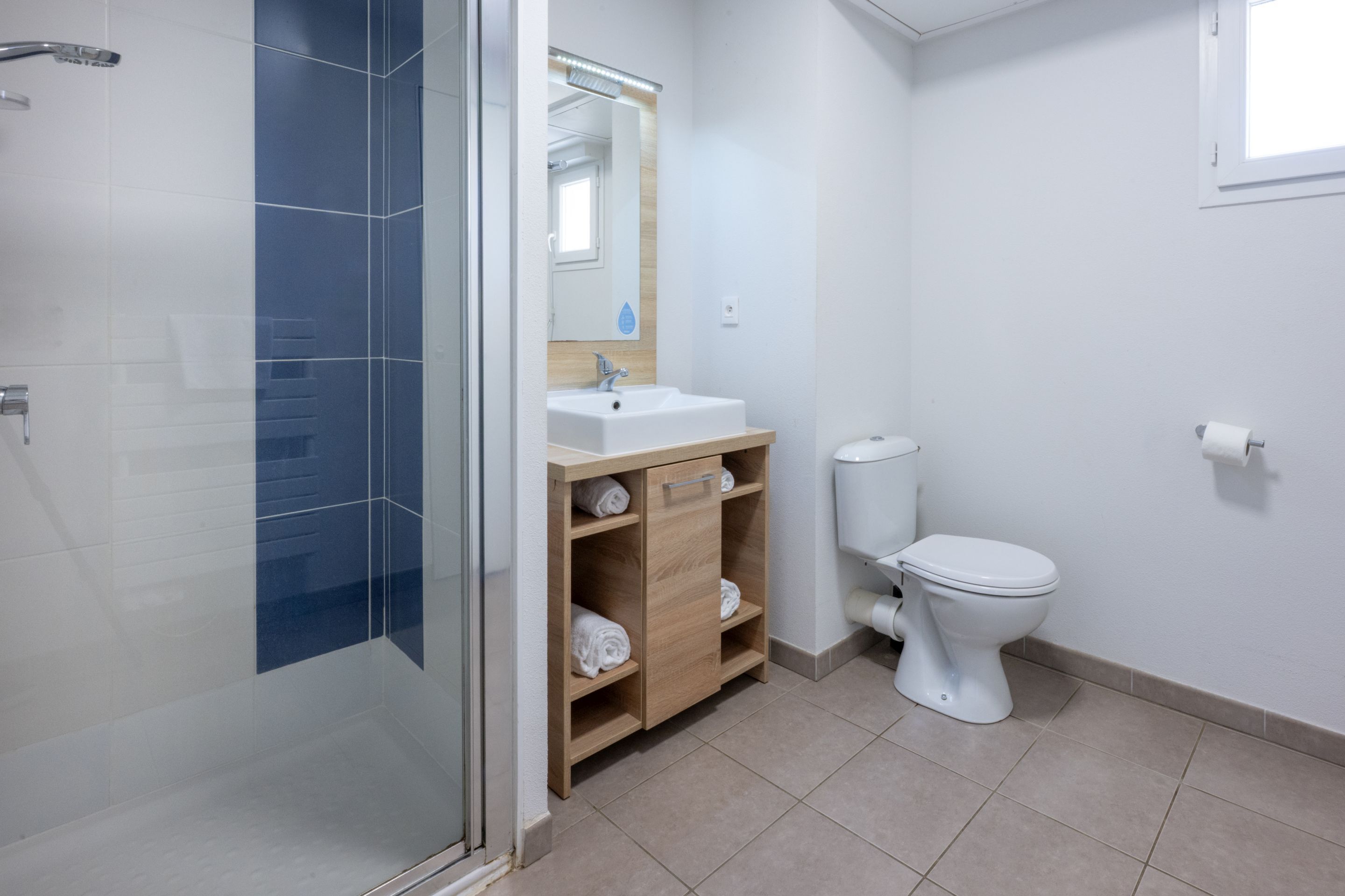 A modern bathroom with a glass shower enclosure, a white sink with a wooden vanity, and a white toilet.