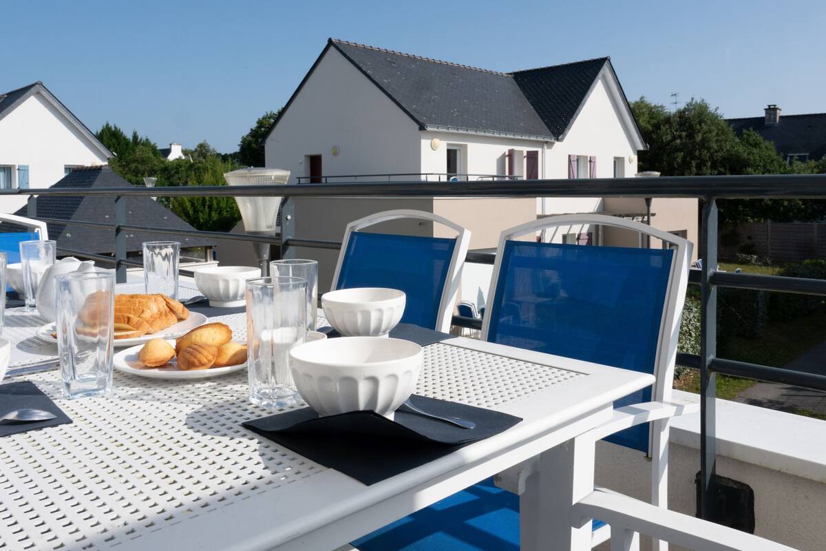 Een eettafel gedekt met borden, glazen en een croissant, met uitzicht op een woonwijk met huizen.