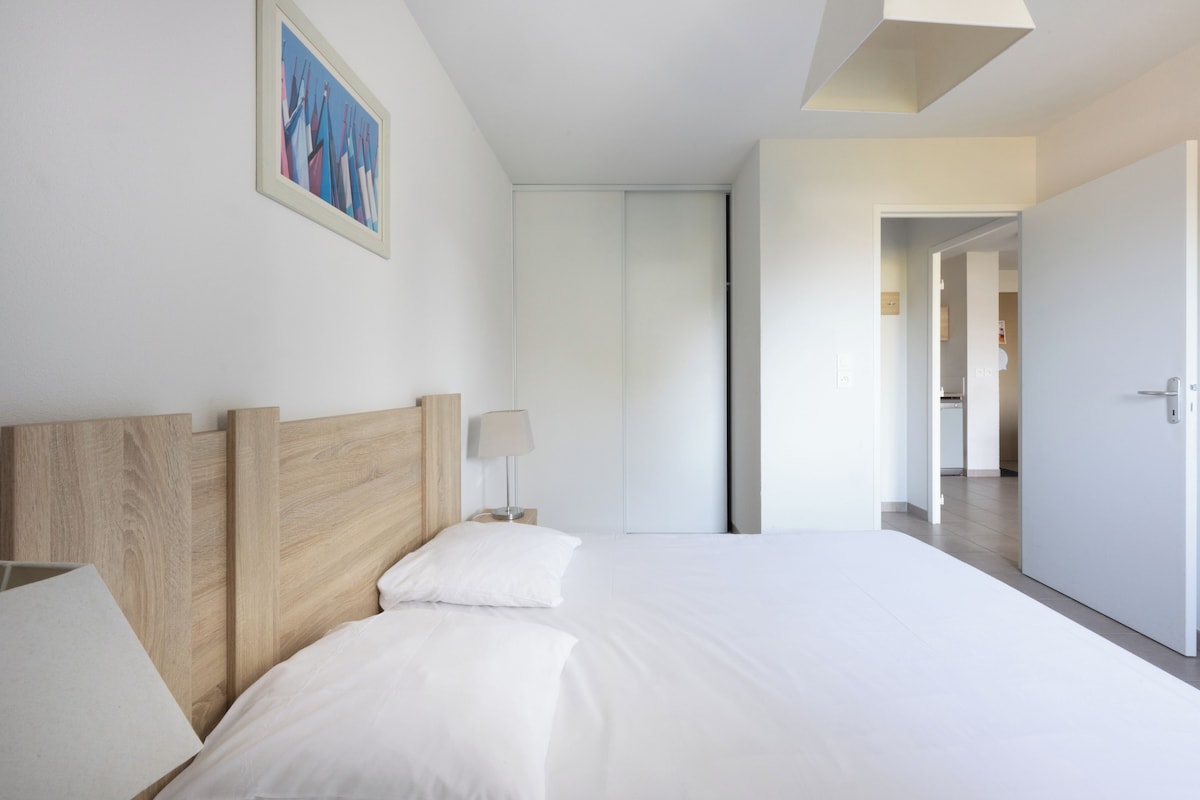 Una habitación de hotel moderna con cabecera de madera, una cama grande, una mesita de noche con lámpara y un cuadro en la pared.