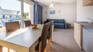 A modern kitchen with a dining area, a sofa, and a view of the outside. - Résidence Odalys Les Iles du Morbihan (Baden)