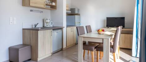 Een moderne keuken met houten kastjes, een ingebouwde magnetron en een koffiezetapparaat. Er is een eethoek met een tafel en stoelen, en een televisie op de achtergrond.