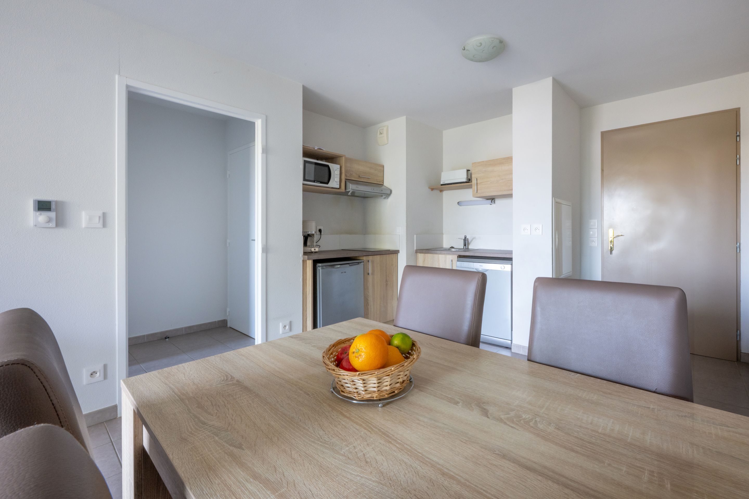 Een moderne keuken met inbouwapparatuur, een eethoek met een houten tafel en stoelen, en een mand met fruit op de tafel.