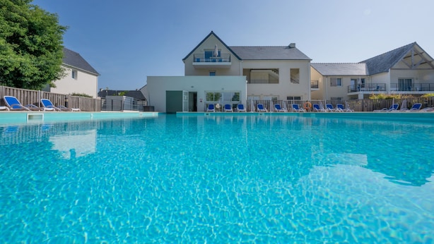 A clear blue swimming pool with lounge chairs and a building in the background. - Résidence Odalys Les Iles du Morbihan (Baden)