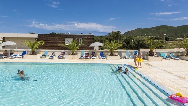 A swimming pool with clear blue water, lounge chairs, and umbrellas. - Résidence Odalys Les Villas de Bel Godère (Belgodere)