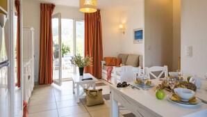 A bright, modern kitchen with a dining area, white furniture, and a view of the outdoors. - Résidence Odalys Les Villas de Bel Godère (Belgodere)