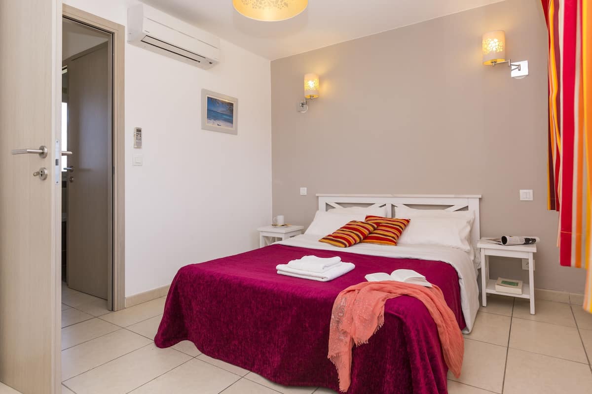 A hotel room with a bed, a nightstand, a wall-mounted lamp, and a door.