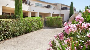 A building with multiple balconies, a gravel pathway, and well-maintained hedges. - Résidence Odalys Les Soleils du Luberon (Bonnieux)