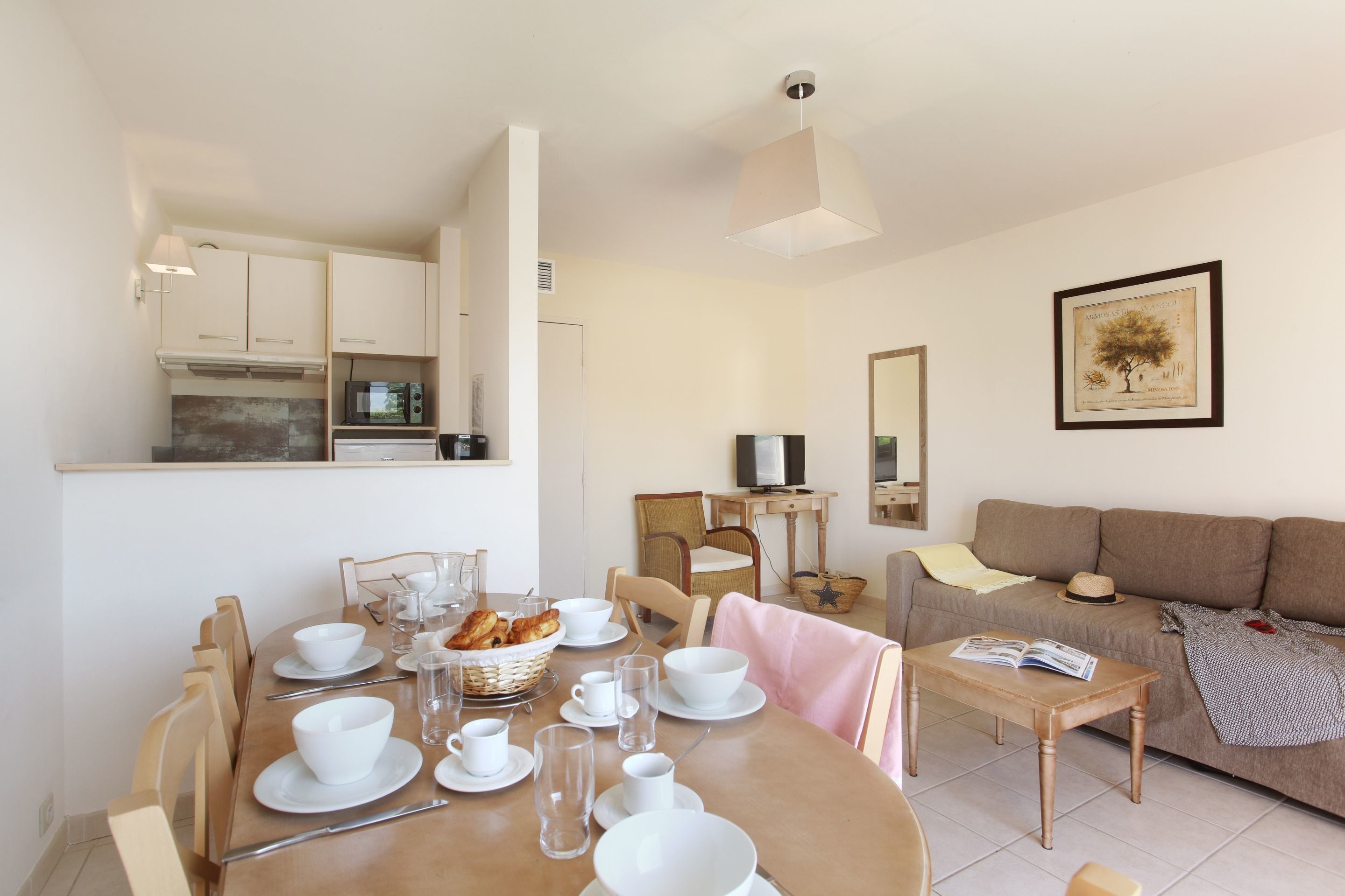 A dining area with a wooden table set for four, surrounded by chairs, and a kitchen area with cabinets and appliances.