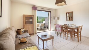 A living room with a sofa, a table, and a dining area with chairs and a table set. - Résidence Odalys Les Soleils du Luberon (Bonnieux)