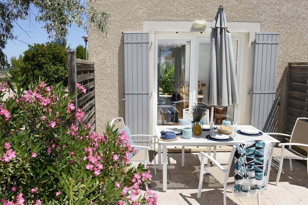 An outdoor patio with a table set for dining, surrounded by white chairs and a wooden fence.