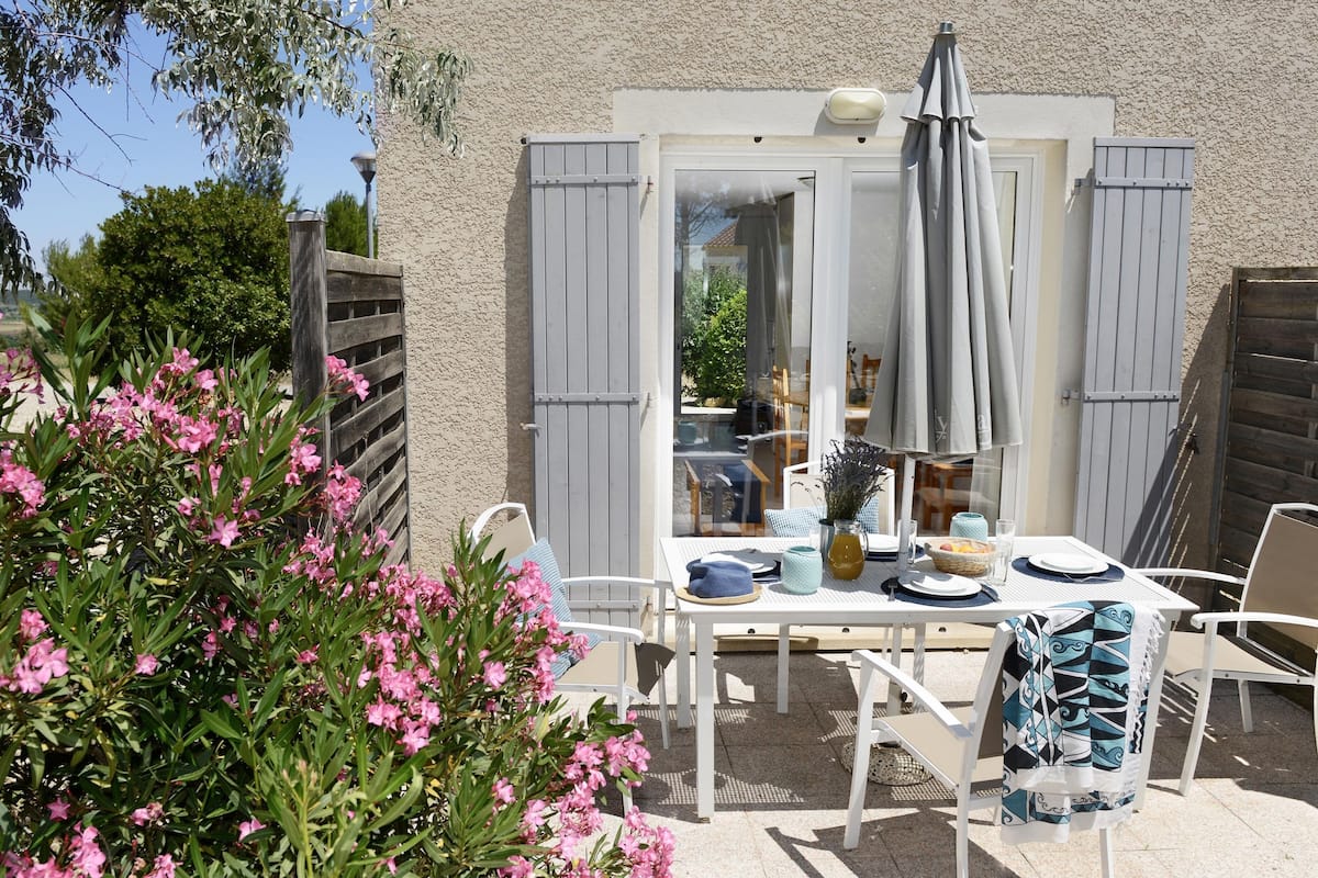 Un patio al aire libre con una mesa lista para comer, rodeado de sillas blancas y una valla de madera.