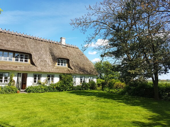 A thatched-roof house with a well-maintained lawn and a large tree in the foreground.