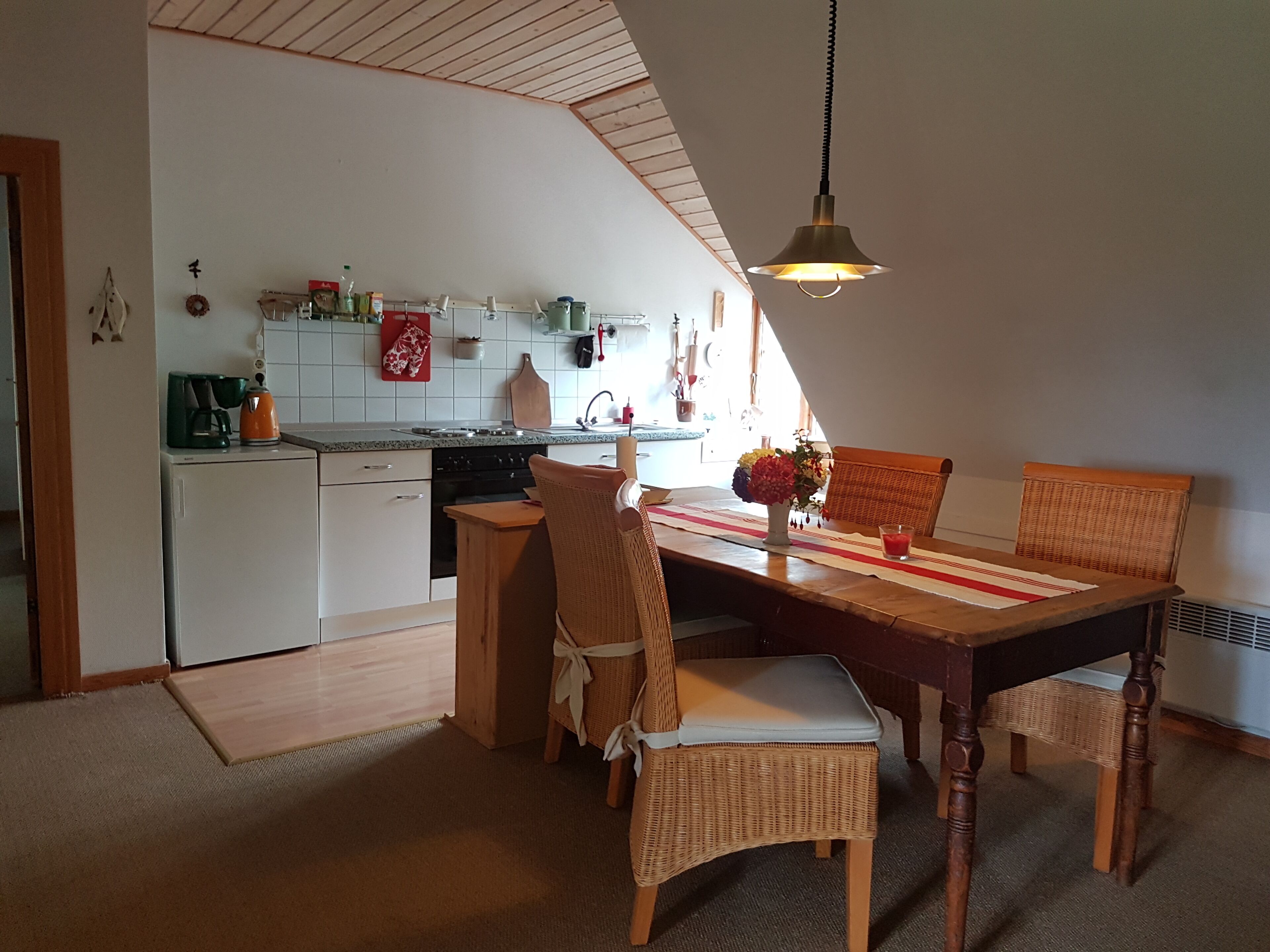 Un coin repas accueillant avec une table en bois, des chaises en osier et un luminaire suspendu.
