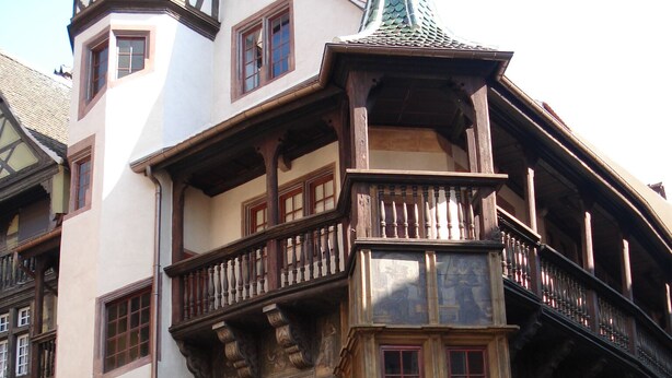 Un edificio histórico con un balcón en esquina, arcos en las puertas y una torre de reloj.