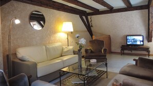 Una sala de estar con un sofá, sillones, una mesa de centro de vidrio, un televisor y una lámpara.