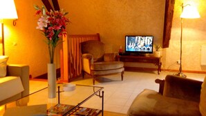 Una sala de estar acogedora con televisor, una butaca, un sofá y un jarrón de flores.