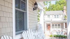 A porch with two white Adirondack chairs, a white picket fence, and a window with blinds. - CORNER BEACH HOUSE (Cape May)
