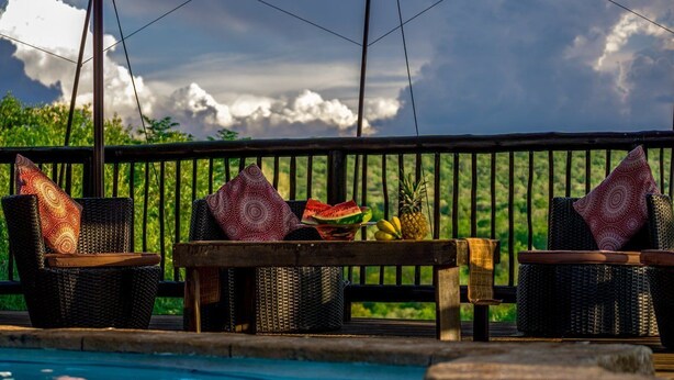 Uma área à beira da piscina com cadeiras de vime e uma mesa com frutas, incluindo uma melancia.