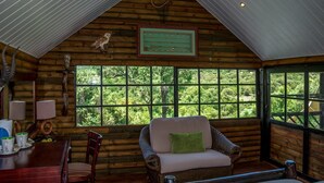 Interior de cabana de toras com área de jantar, um banco acolchoado e grandes janelas com vista para a floresta.
