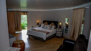 Quarto com cama, mesas de cabeceira, piso de madeira, sofá de couro e vista para o verde lá fora.