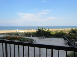 Uitzicht op een strand vanaf een balkon met een balustrade, een zandstrand en de oceaan op de achtergrond.