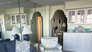 A living room with a blue sofa, patterned armchair, and ottoman, a patterned rug, and a kitchen with white cabinets and a fish-shaped soap dish. - Magnificent Ocean Front. Beautiful five-star. Perfect, quiet get-away. (Bethany Beach)