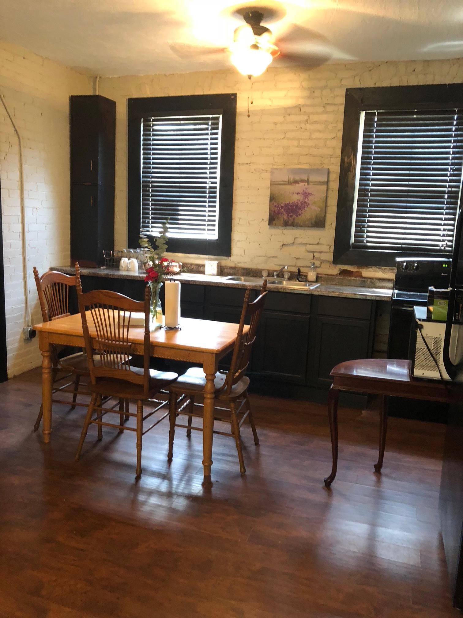 A kitchen with a dining table, chairs, a ceiling fan, and two windows with blinds.