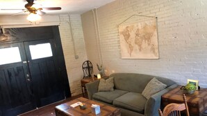 Een gezellige woonkamer met een groene bank, een houten salontafel, een wereldkaart aan de muur en een zwarte deur.