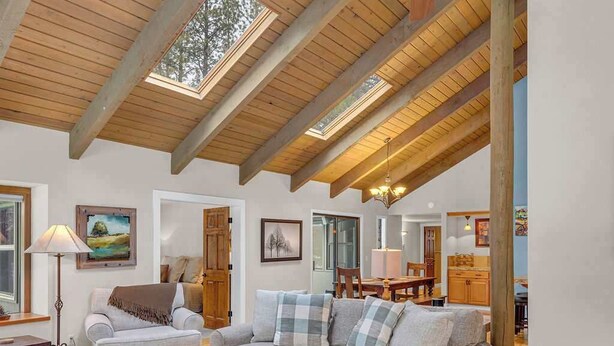 A spacious living room with a high ceiling, wooden beams, a ceiling fan, and a large window. - Unique spacious cabin with private deck, hot tub! (Sunriver)