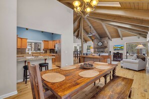 A spacious kitchen with wooden cabinets and a large island, a dining area with a wooden table and chairs, and a living room with a sofa and a view of the outdoors.