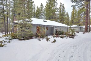 A cabin with a snow-covered roof, surrounded by tall pine trees.