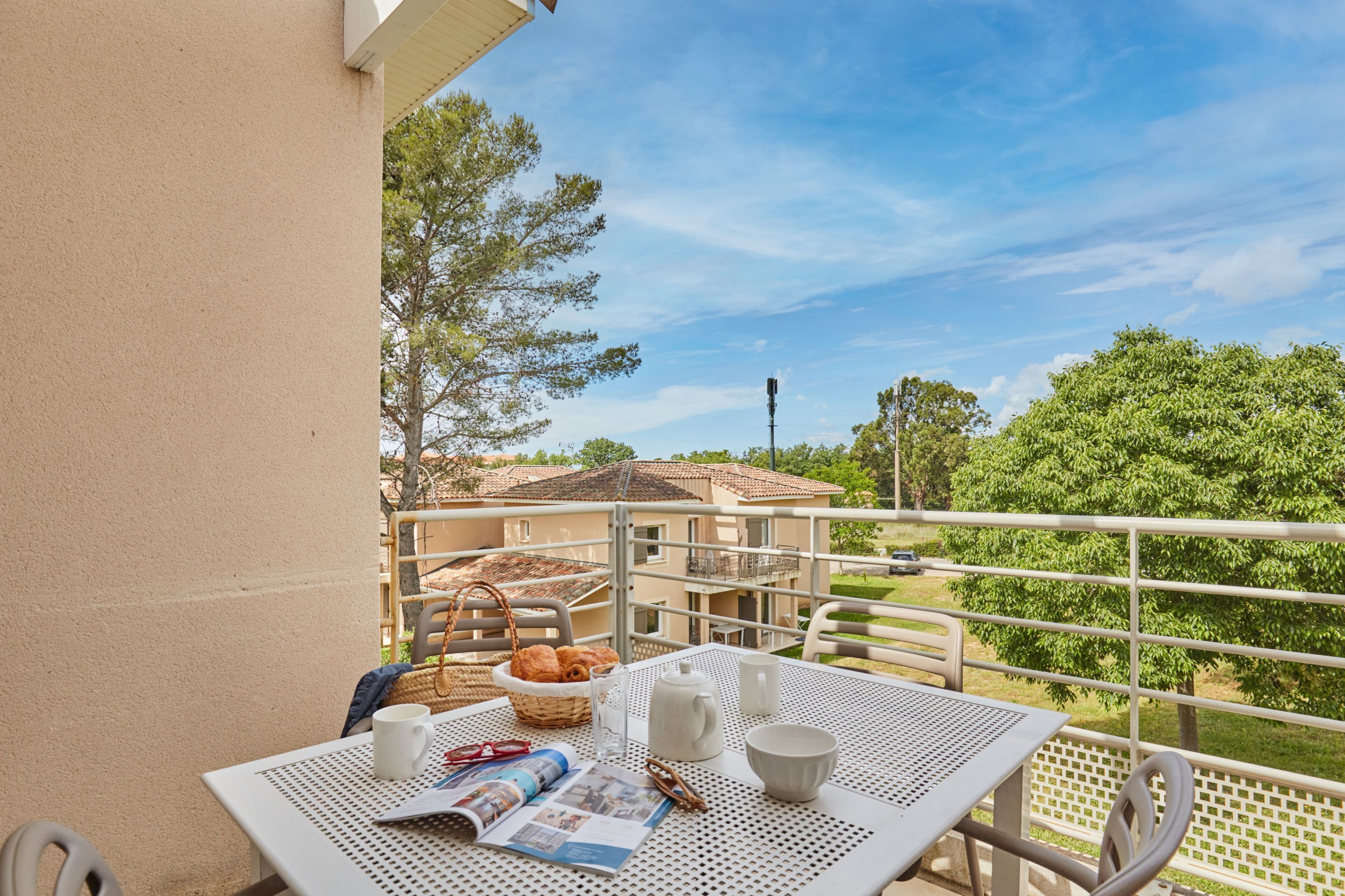 Ein Balkon mit Frühstückstisch, komplett mit Brot, einer Zeitung und einer Tasse.
