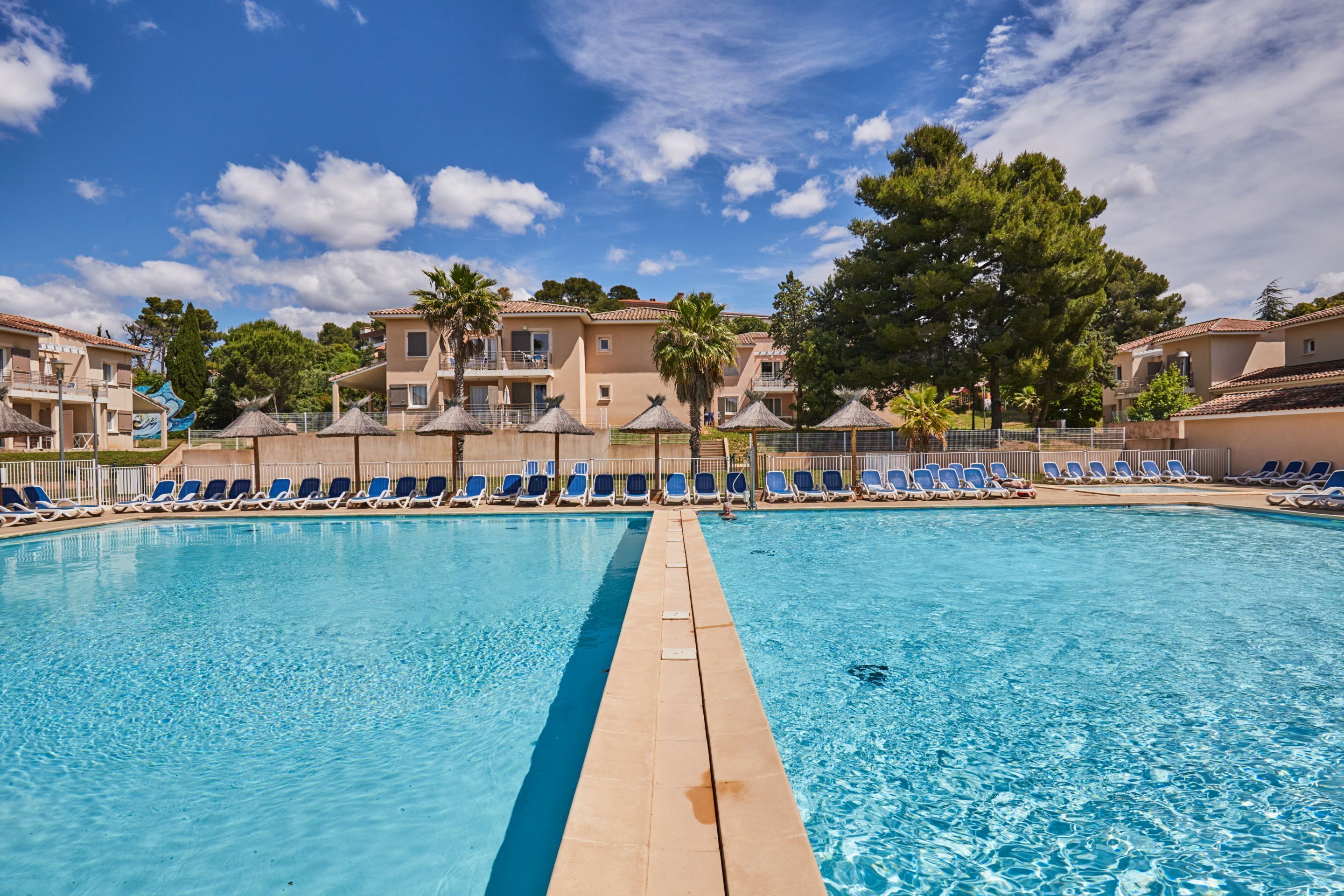 A swimming pool with blue lounge chairs and a clear sky.